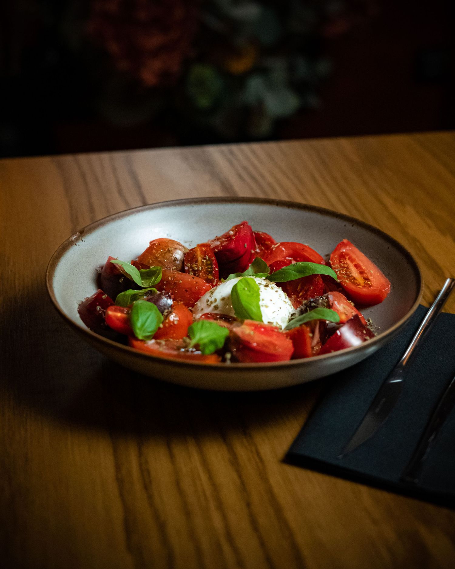 Fresh caprese salad with cherry tomatoes, burrata cheese, and basil leaves in a rustic ceramic bowl on wood table.
