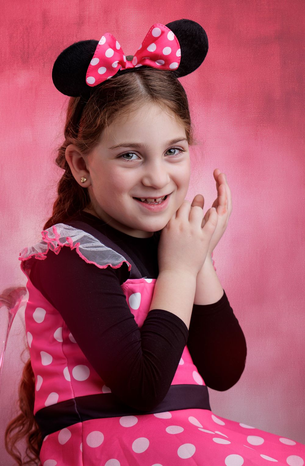 Young girl smiling in pink Minnie Mouse costume with polka dots and ears on pink background.
