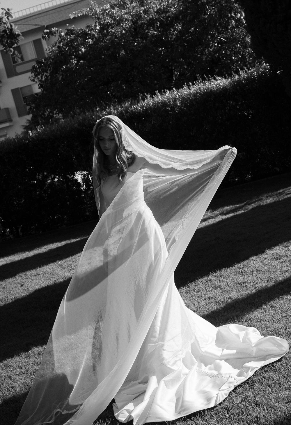 Bride in flowing white wedding gown and veil caught by wind outdoors, elegant black and white bridal portrait.