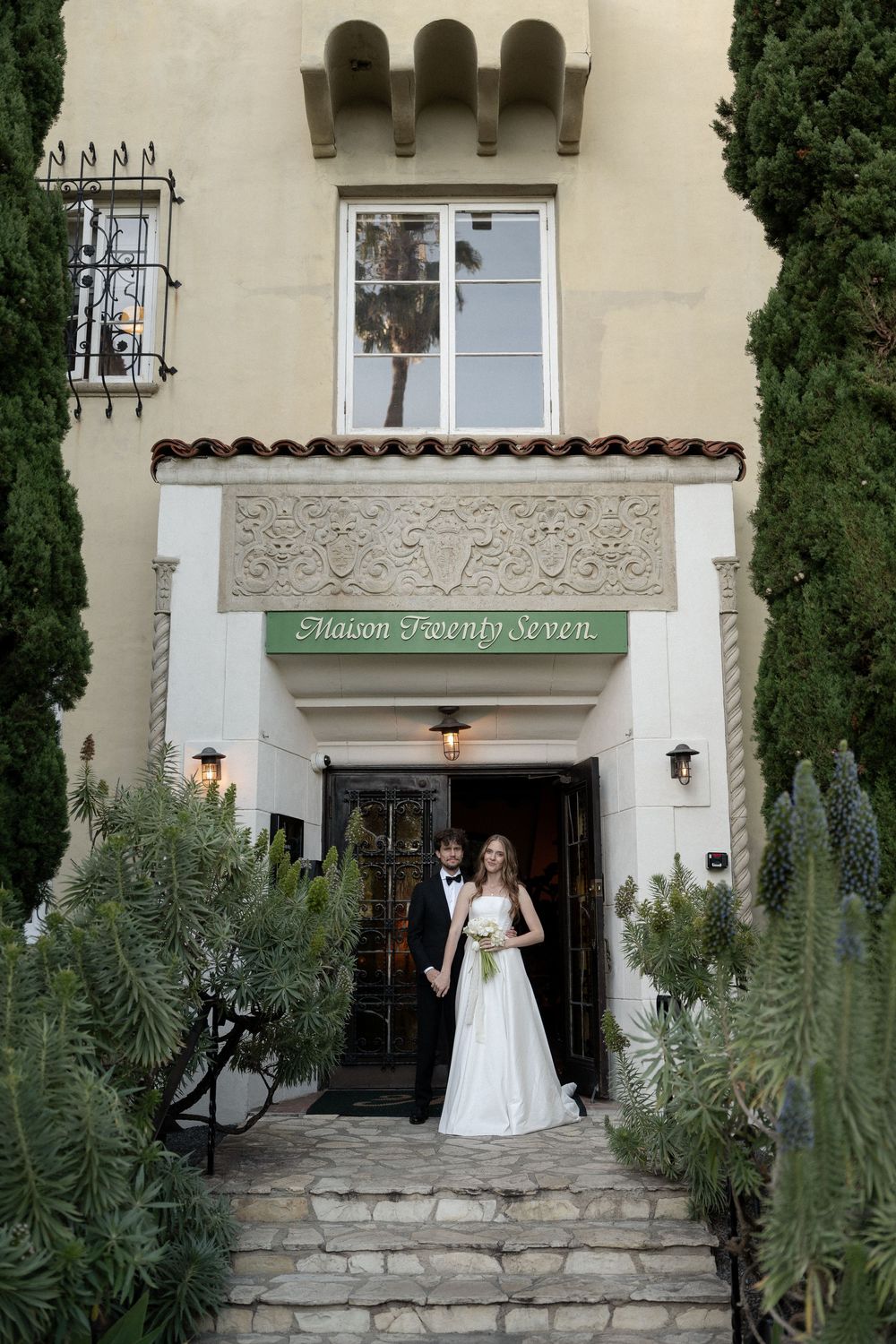 Bride and groom posing at entrance of Maison Twenty Seven venue on their wedding day.