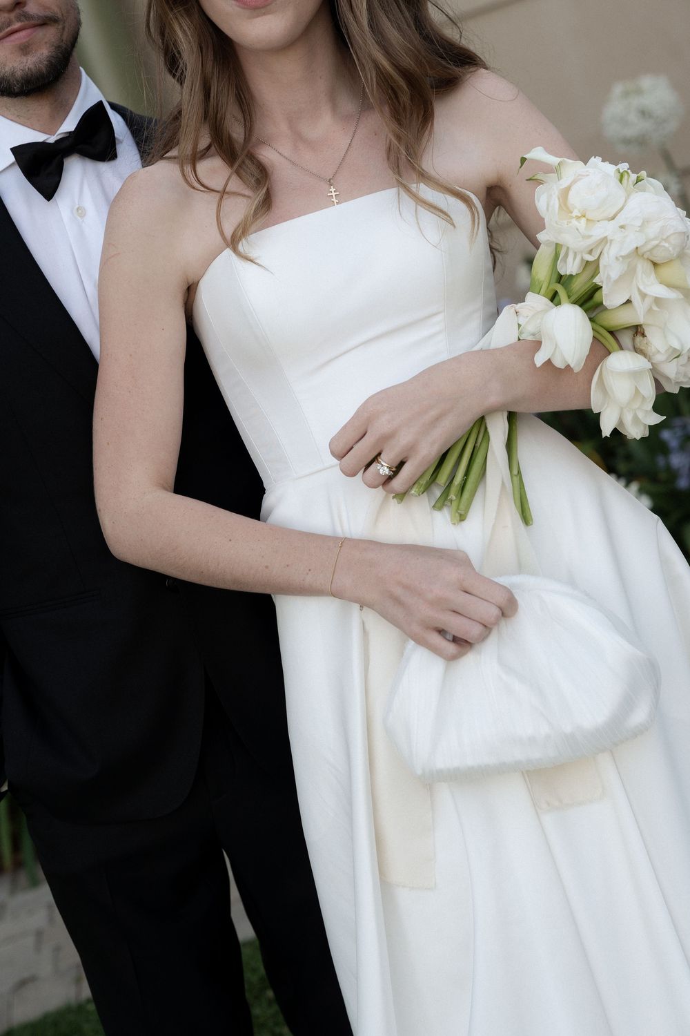 Bride in strapless white gown holding white tulip bouquet with groom in black tuxedo.