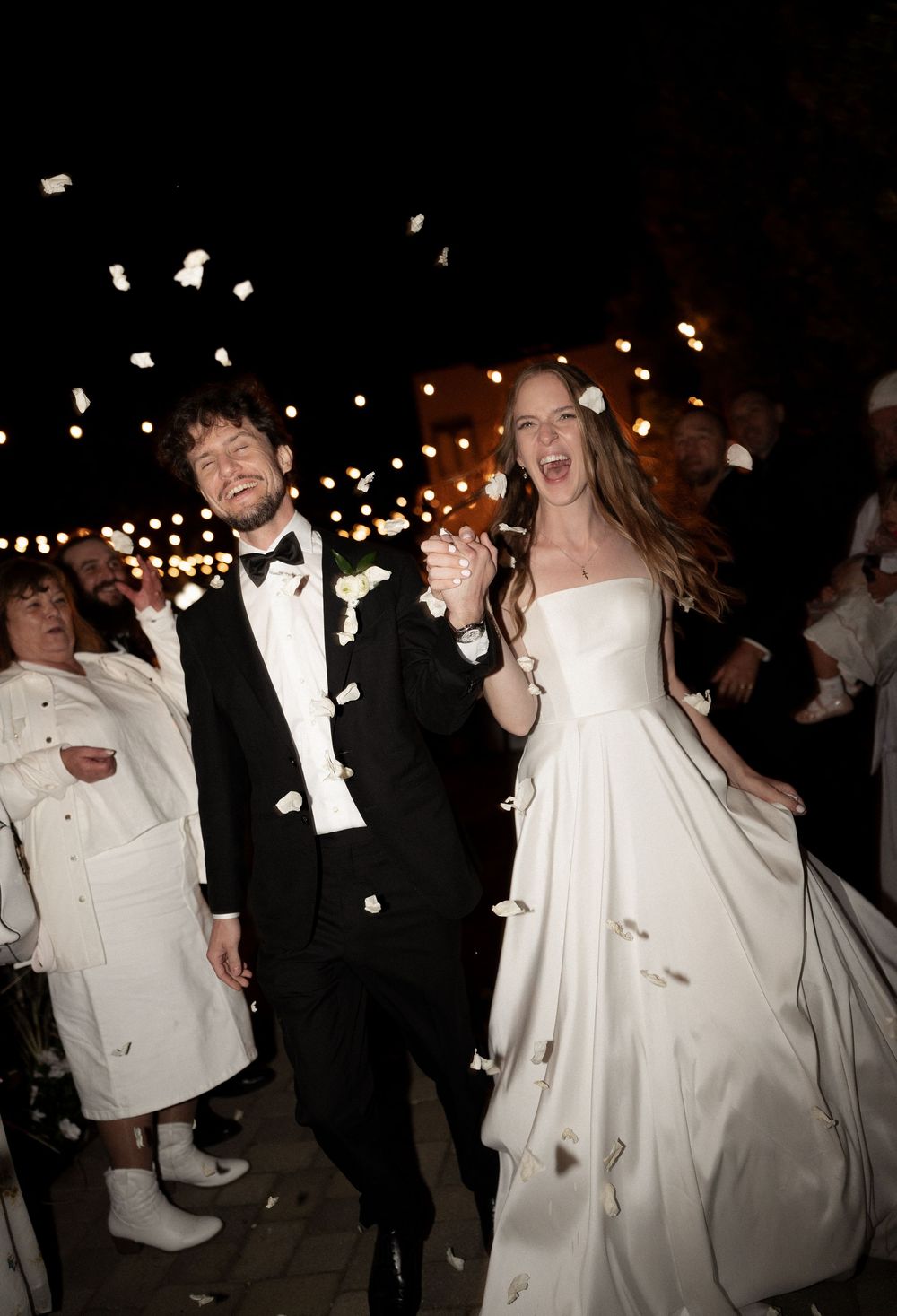 Joyful newlyweds celebrating grand exit with confetti shower at night wedding reception.