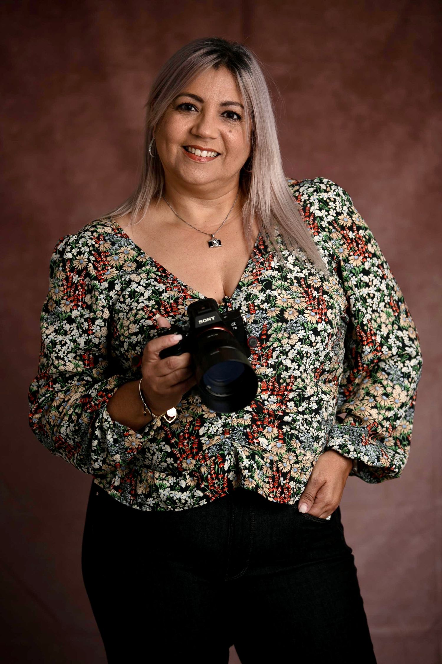 Smiling woman with gray highlighted hair wearing a black and white graphic design print top and gold jewelry.