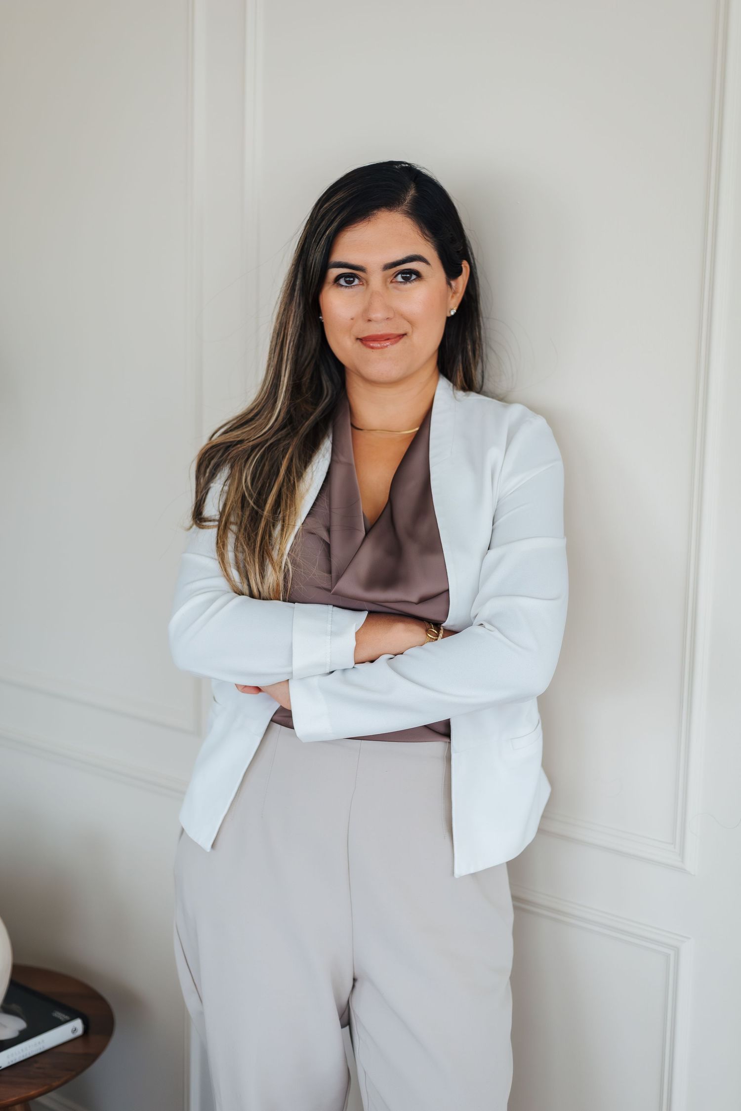 A woman in business stands confidently with arms crossed leaning against a wall for headshots. Alberta wedding and branding photographer.