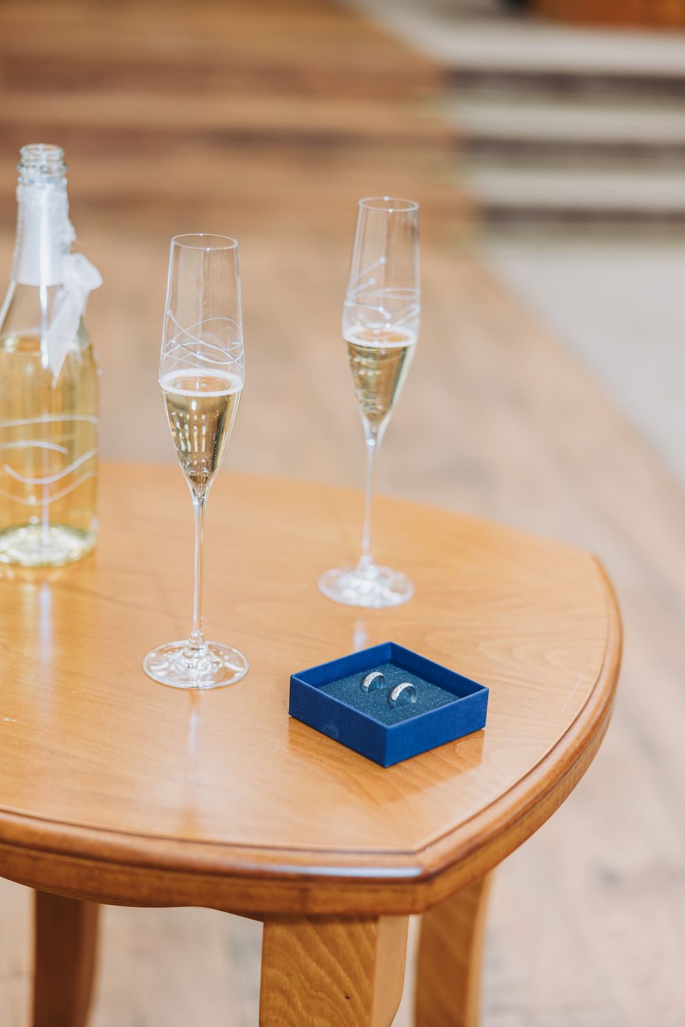 Two champagne flutes and wedding rings in a blue box on a wooden table, perfect for a romantic celebration.