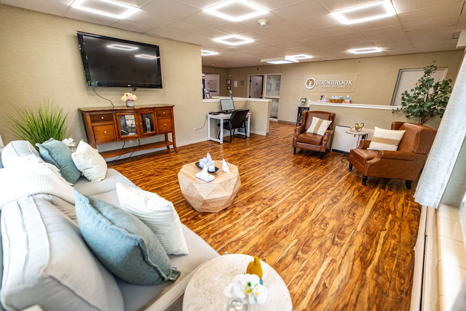 Modern living room with hardwood floors, white sofa, leather chair, and wall-mounted TV.