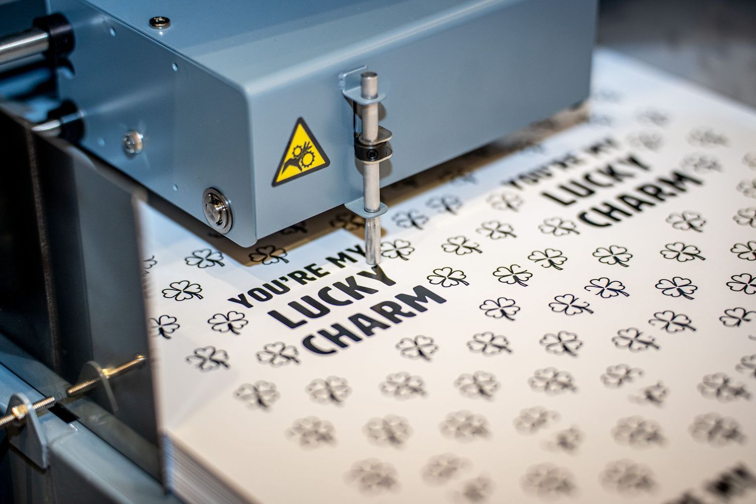Laser engraving machine cutting lucky charm text and paw print patterns onto white material.