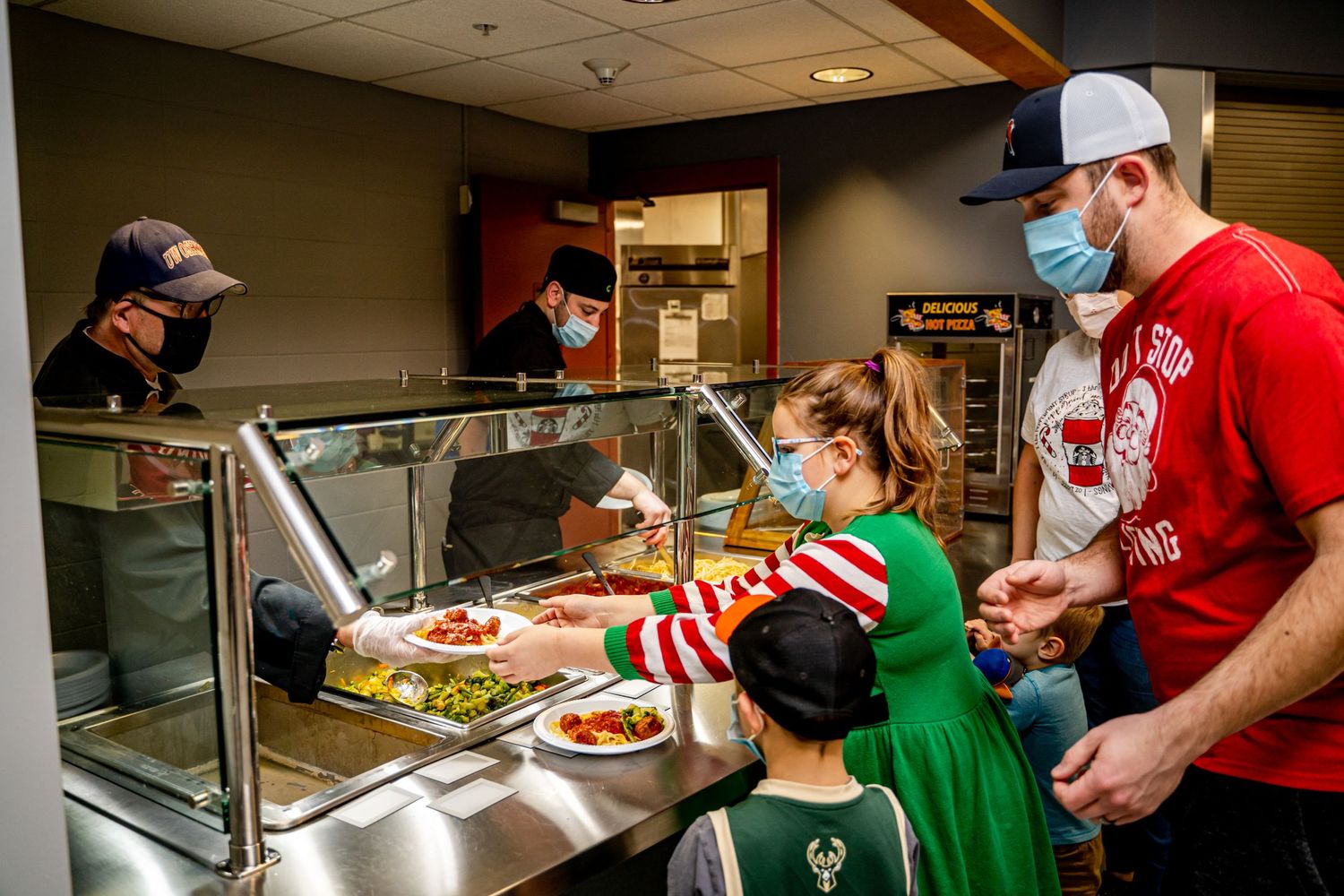 Family being served food at a cafeteria-style counter while wearing protective face masks.