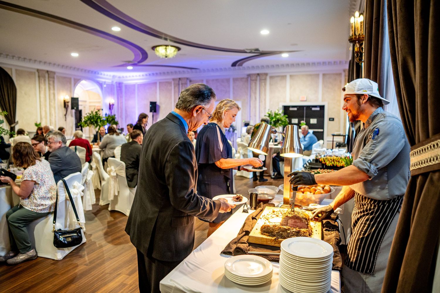 Guests serving themselves at a catered buffet dinner in an elegant banquet hall during a formal event.