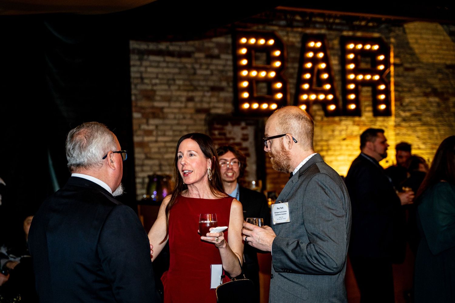 Guests socializing at a bar event with illuminated BAR sign in background.