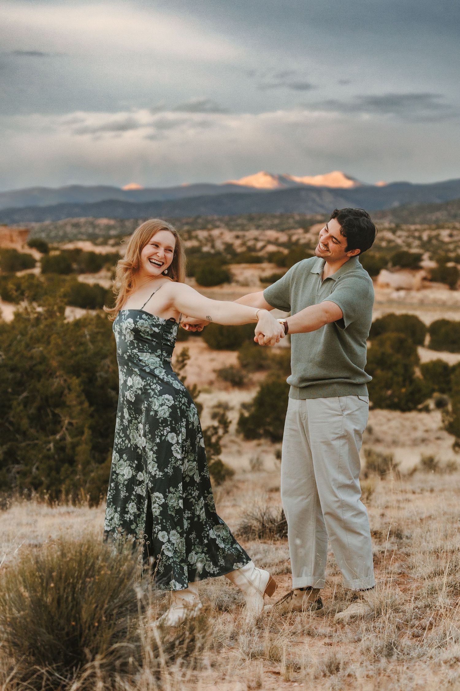 A joyful couple dances outdoors in a desert landscape with mountains and dramatic sunset sky behind them.