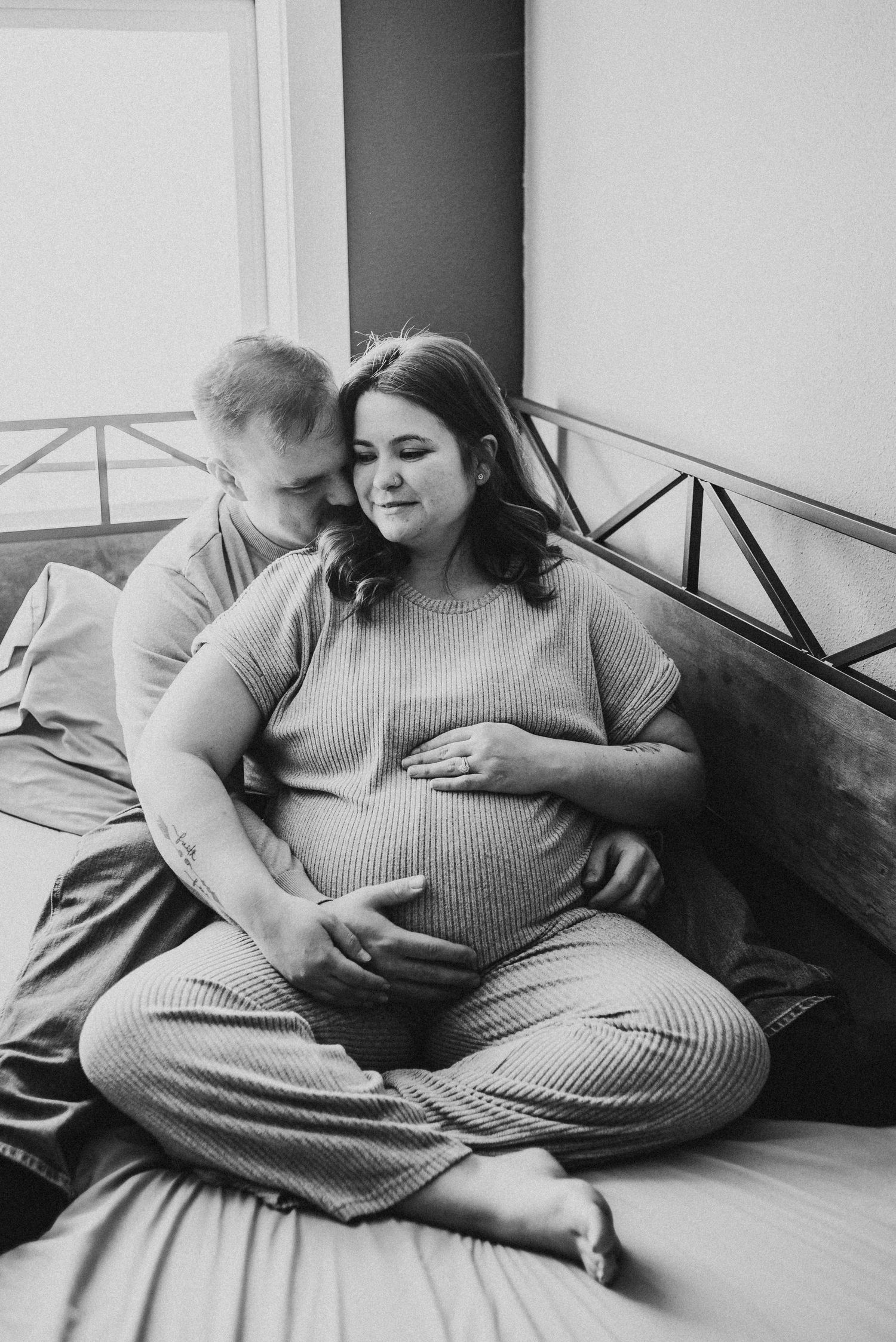 Expecting couple sitting together on a bed during an in-home maternity session