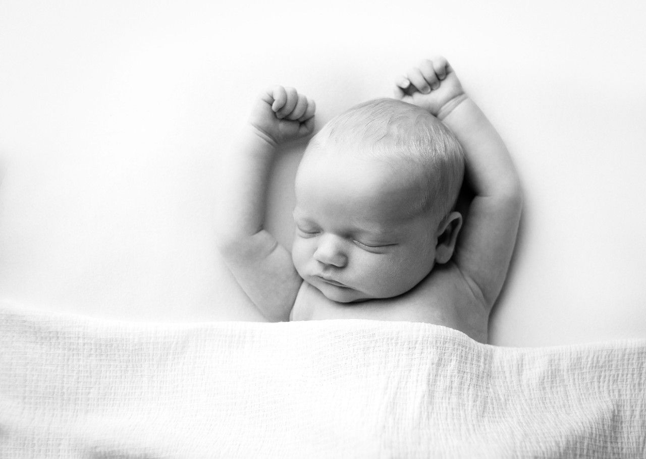black and white image of sleeping newborn with arms stretched up