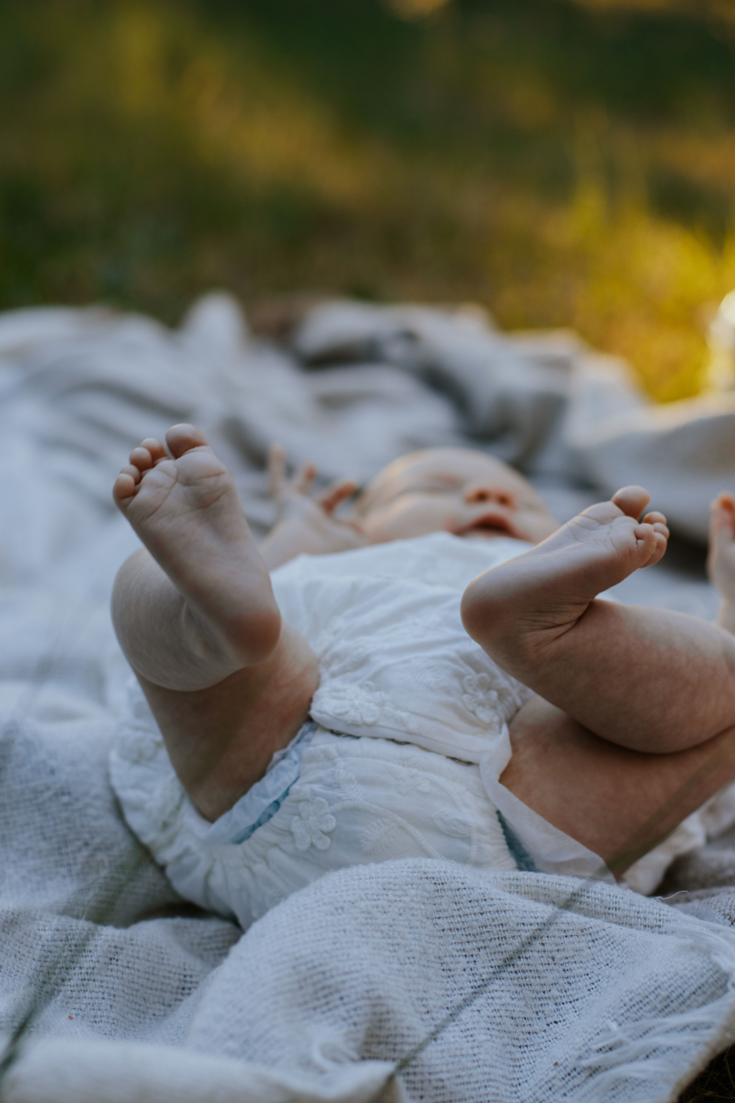 Close-up of tiny newborn baby feet resting on a soft white blanket outdoors in natural light.