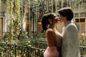 Couple sharing a romantic moment on a balcony surrounded by lush greenery and hanging vines at an elegant venue.