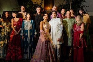 Bride and groom in traditional Indian wedding attire pose with family and guests in colorful ethnic outfits.