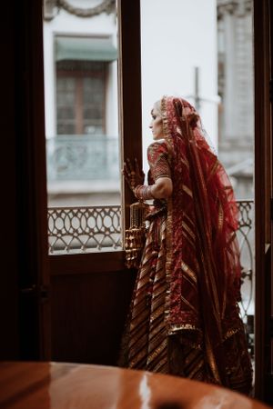 A traditional red bridal veil and outfit seen through window panes in moody lighting.