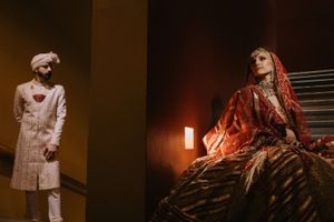 South Asian bride in red lehenga and groom in white sherwani pose separately in dramatic wedding portrait.
