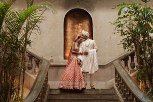 Wedding couple photographed against a neutral wall with tropical plants.