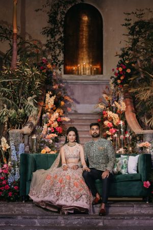 Elegant wedding setup with floral arrangements and green velvet seating against a romantic evening backdrop.