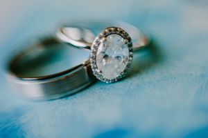 Close-up of elegant diamond engagement rings and wedding bands on blue surface.