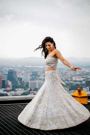 A sparkling white lehenga twirls against a cityscape backdrop on a rooftop.