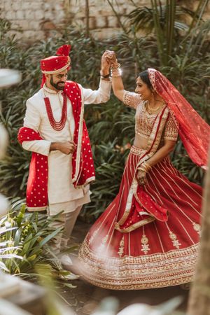 Joyful couple in traditional Indian wedding attire dancing in a garden setting.