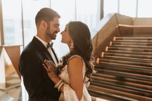 Romantic moment captured between newlyweds in formal attire against a sunlit window backdrop.
