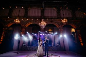 Wide shot of a grand ballroom during a wedding first dance with purple stage lighting.