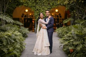 Newlyweds pose together on garden path with arched doorway and ferns in background.