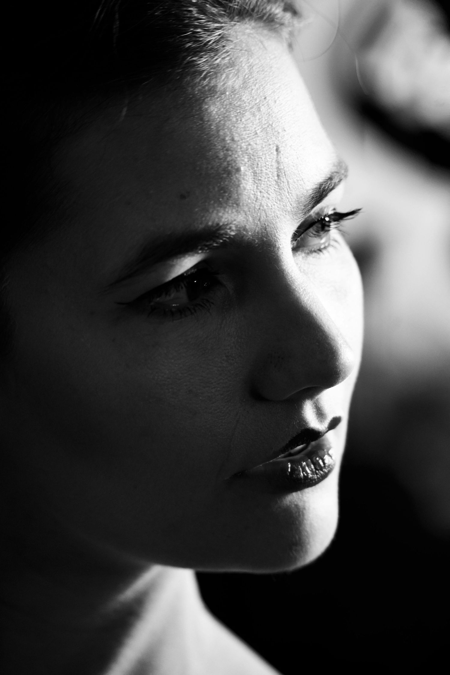Portrait en gros plan, en noir et blanc, d'une jeune femme aux traits saisissants, le regard pensif tourné sur le côté.