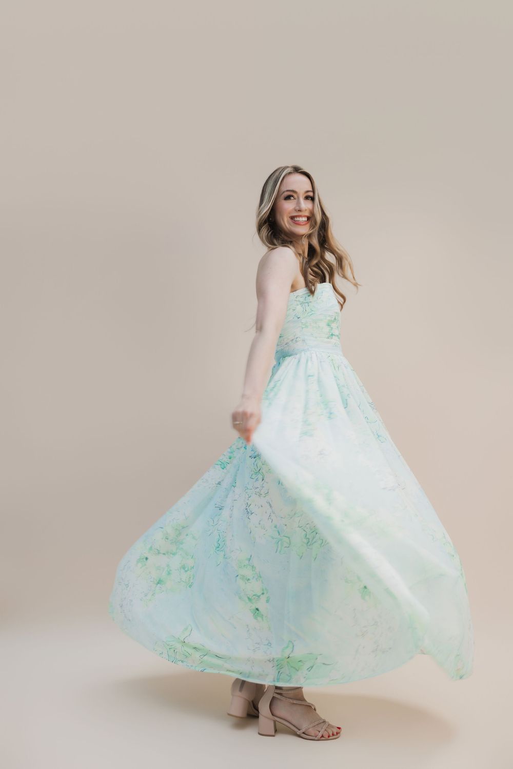 Woman twirling in a mint green floral maxi dress, smiling over her shoulder against a beige background.