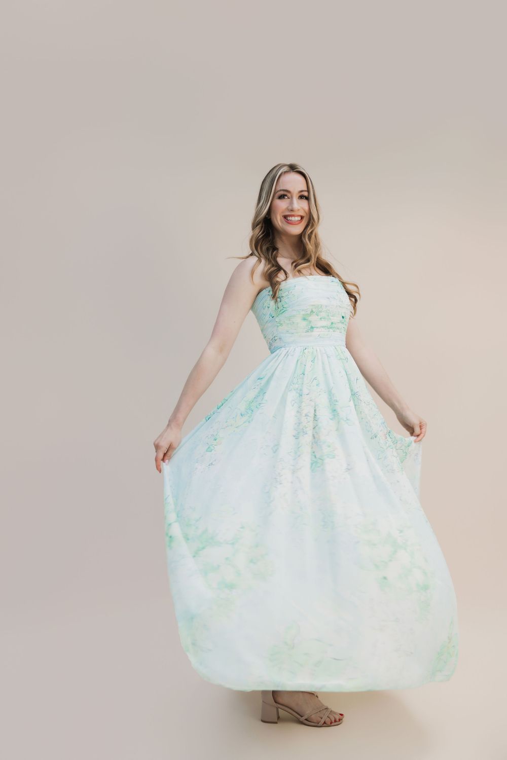 Woman twirling in a floral mint green strapless ball gown, smiling in a studio setting.