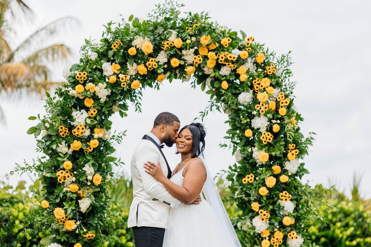 Romantic outdoor wedding ceremony with palm trees and flowing white veil.