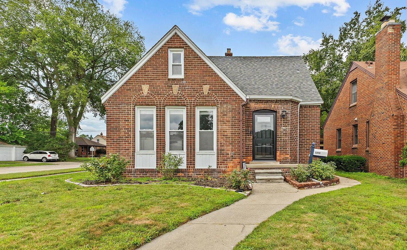 Charming brick bungalow with steep gabled roof, manicured lawn, and classic front entrance surrounded by mature trees.