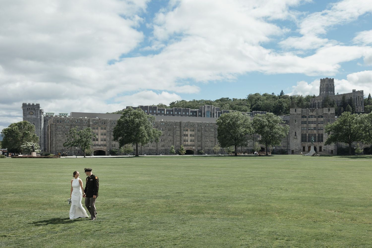 Wedding ceremony setup with white chairs on a lush green lawn facing a historic stone church under cloudy skies.
