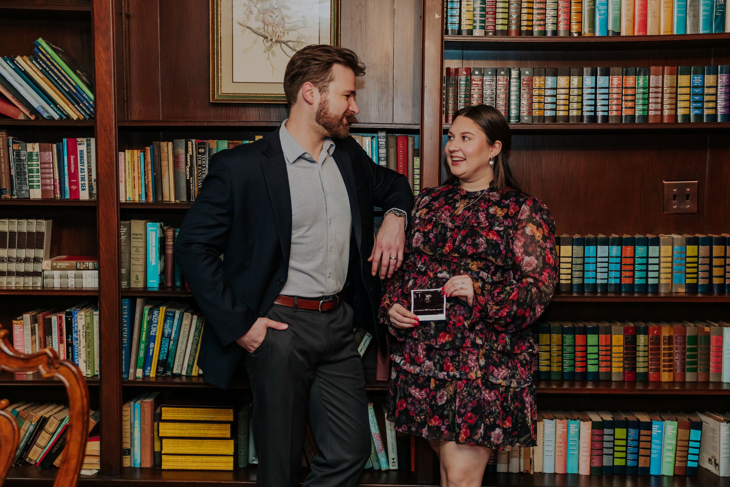 A couple poses together in a library with wooden bookshelves filled with colorful books in the background.