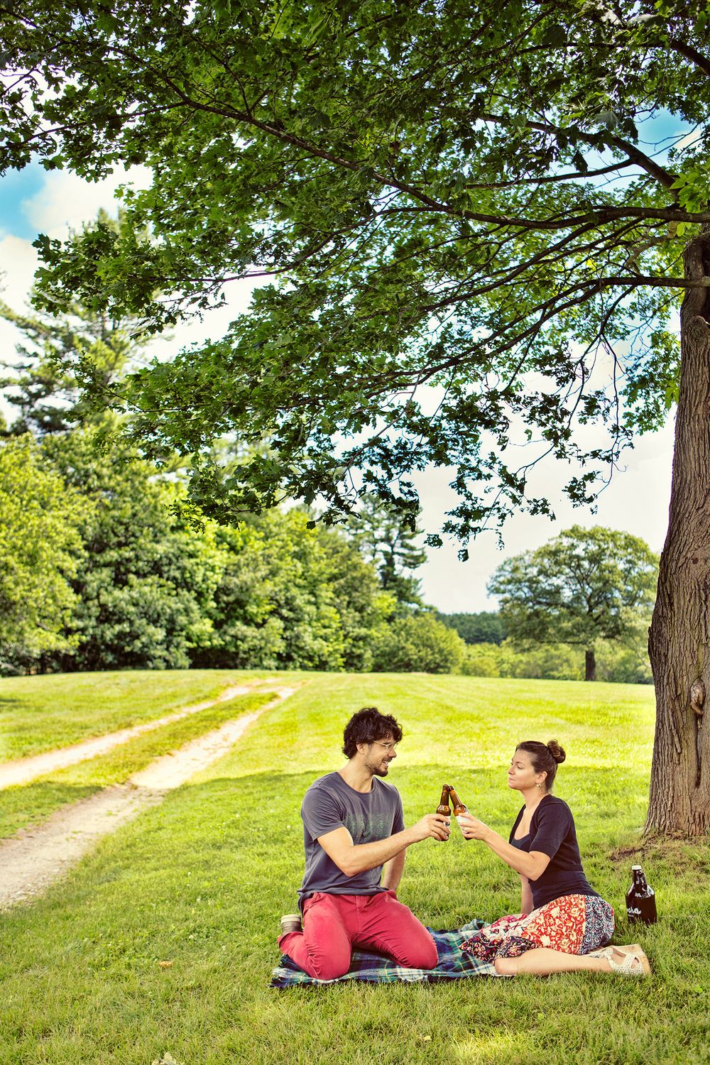 Couple sitting on grass under a tree sharing Boocha Kombucha bottles at a picnic.