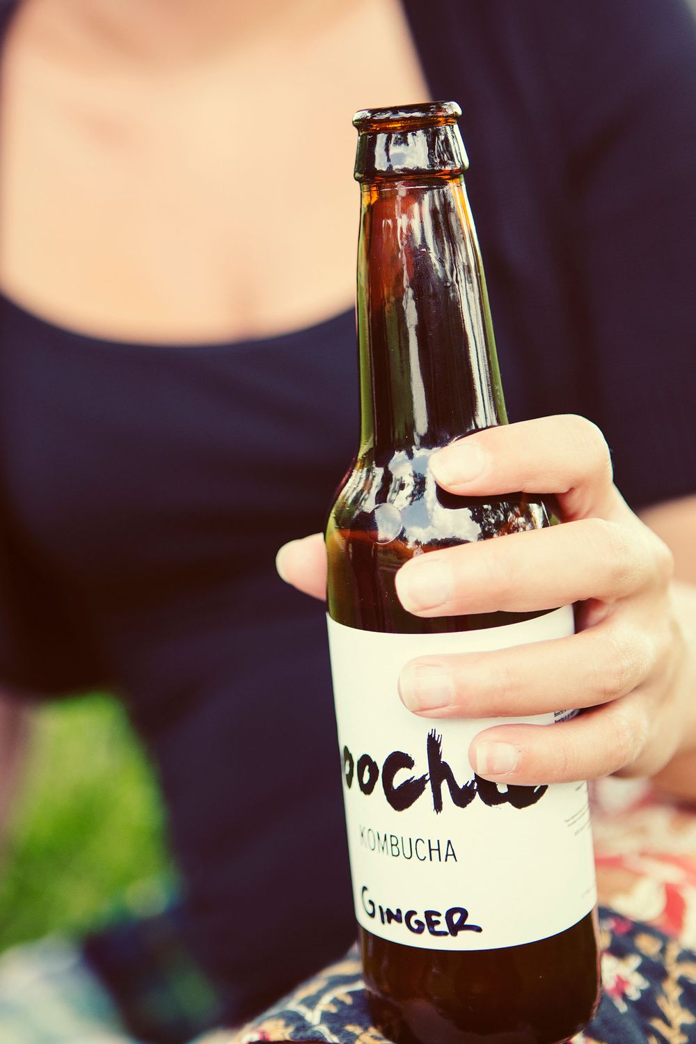 Close-up of a hand holding a Boocha Ginger Kombucha bottle outside.