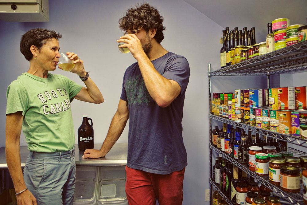 Two people sampling Boocha Kombucha drinks in a pantry stocked with shelves.
