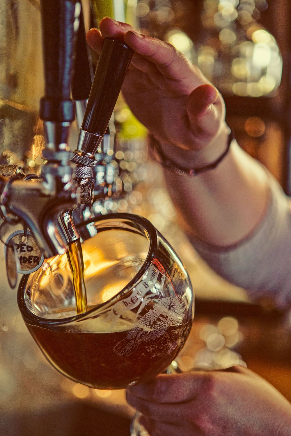 Bartender pouring dark craft beer from tap into a goblet glass at a bar.