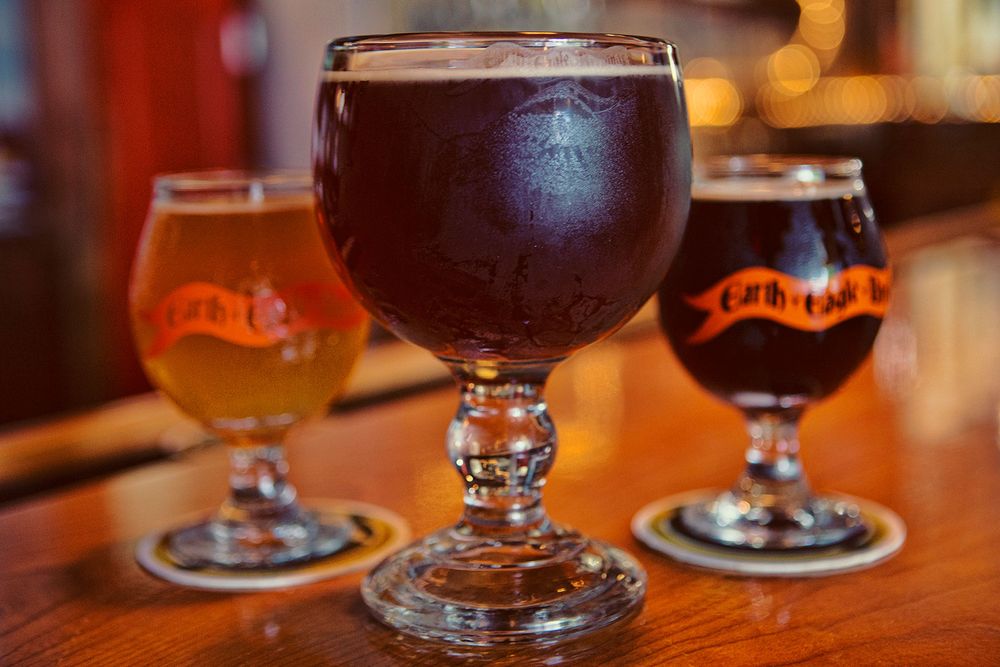 Three craft beer goblet glasses with brewery logo on a wooden bar counter.