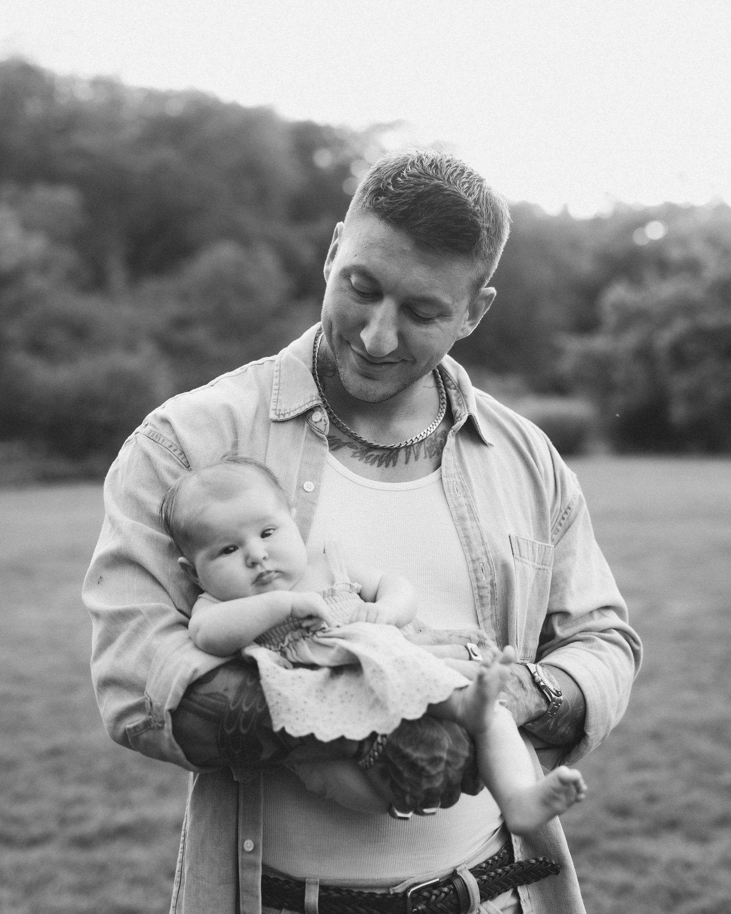 Black and white photo of a man tenderly cradling a newborn baby in an outdoor field.