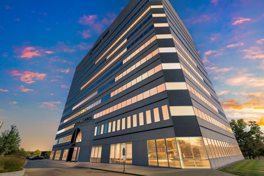 Modern multi-story office building with glass facade illuminated at dusk against a vibrant blue and orange sunset sky.