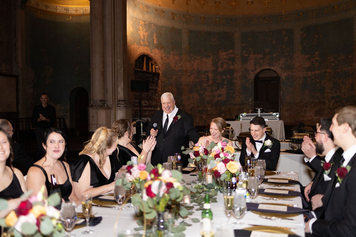 Elegant wedding reception dinner with guests in formal attire seated at decorated tables in a grand ballroom.