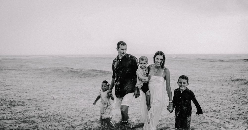 Family of five walking on a beach in black and white, parents and three children splashing in ocean waves.