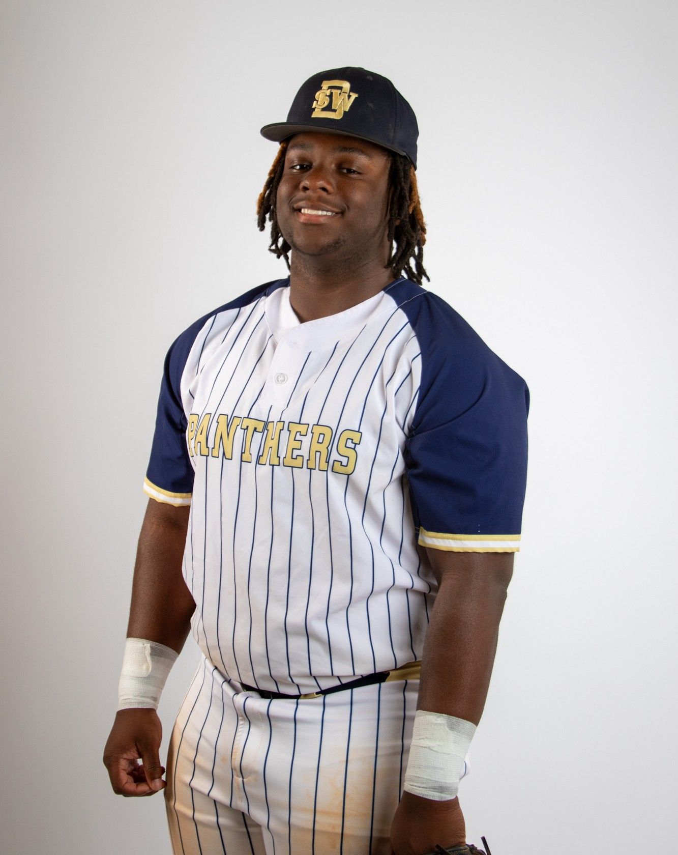 Young baseball player in Panthers pinstripe uniform and navy cap poses for team photo against white background.