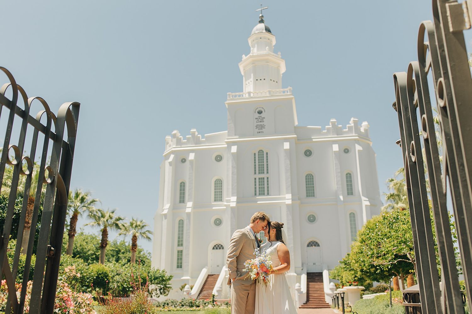 Bride and groom kissing in front of a white LDS temple on a sunny wedding day.