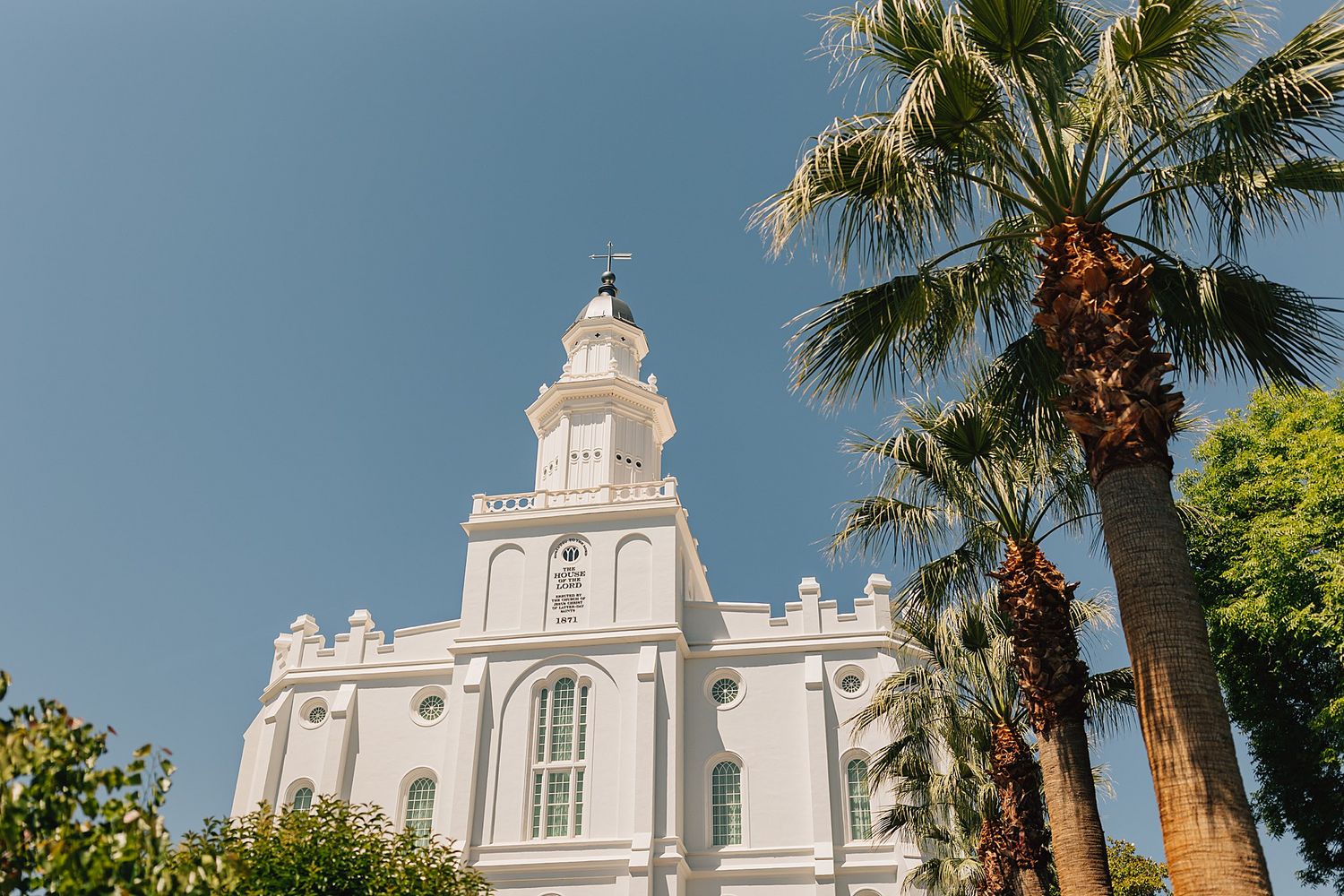 White LDS temple with ornate spire surrounded by palm trees under clear blue sky.