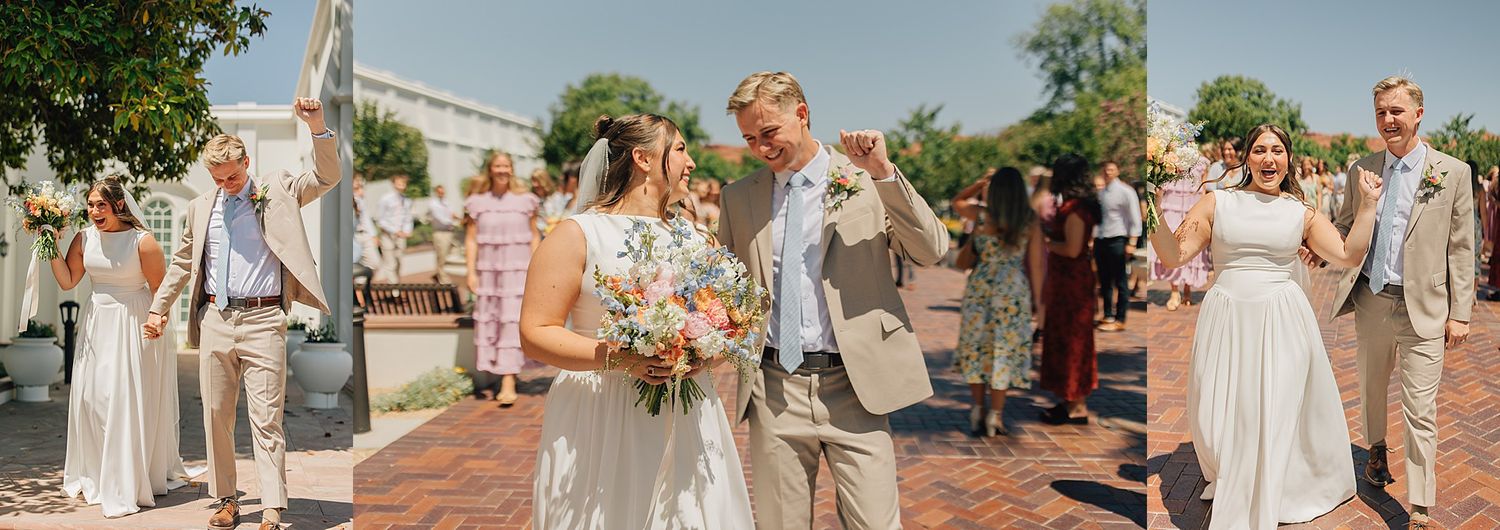 Newlyweds walk joyfully with guests cheering outside bright white wedding venue on a sunny day.